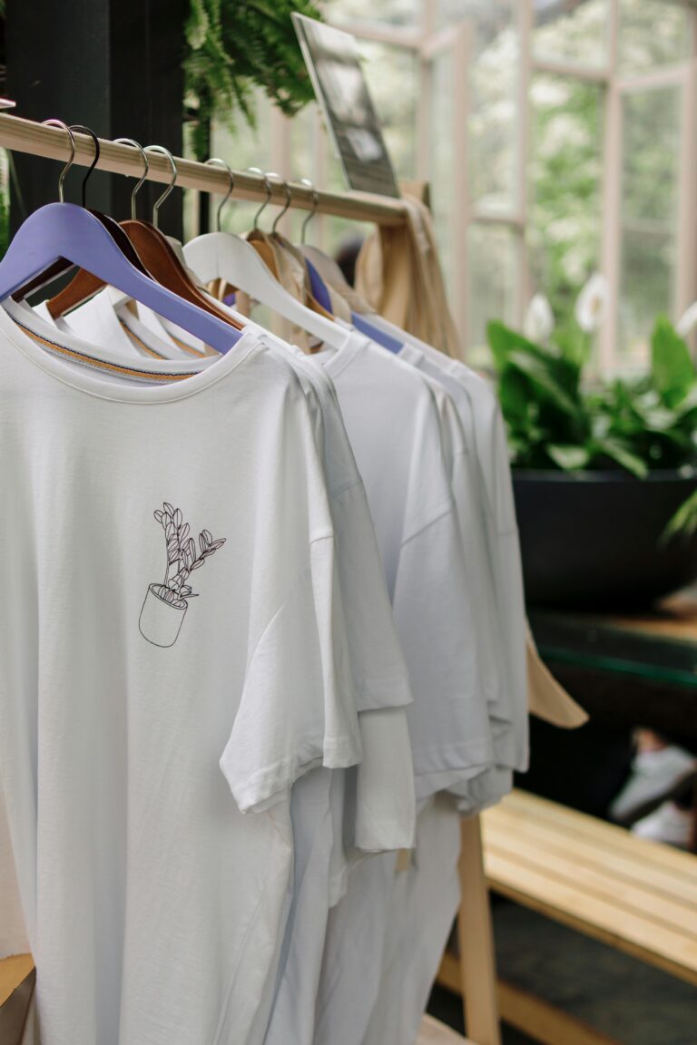 Row of white t-shirts with plant design in a botanical-themed shop interior.